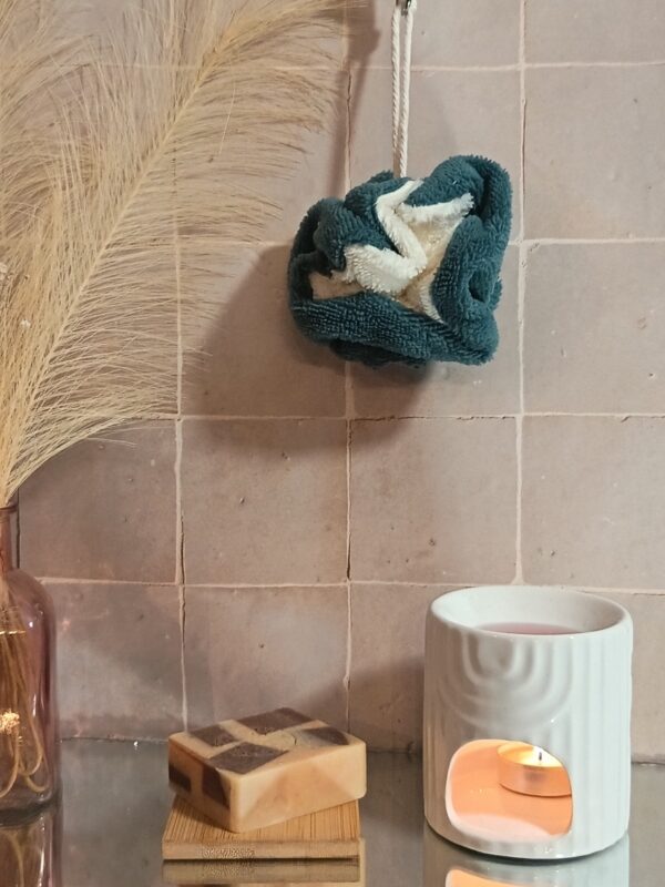 Fleur de douche bicolore en bambou crème et bleu indigo, mise en scène dans une salle de bain zen avec bougie et savon.