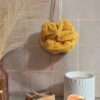 Fleur de bain en bambou coloris jaune moutarde, texture douce et absorbante, suspendue dans une ambiance spa.