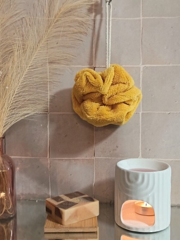 Fleur de bain en bambou coloris jaune moutarde, texture douce et absorbante, suspendue dans une ambiance spa.