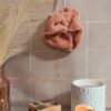 Fleur de bain écologique en fibre de bambou coloris pêche, suspendue dans une salle de bain à l'ambiance zen et naturelle.
