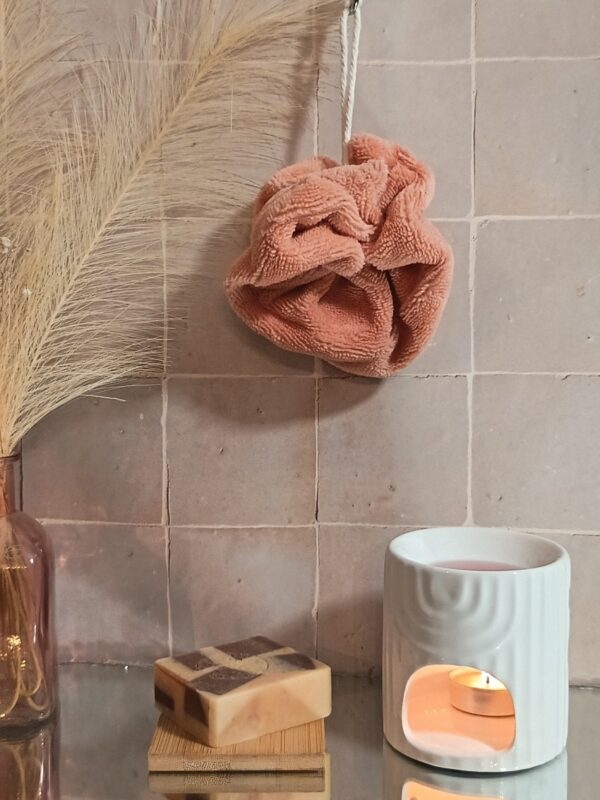 Fleur de bain écologique en fibre de bambou coloris pêche, suspendue dans une salle de bain à l'ambiance zen et naturelle.