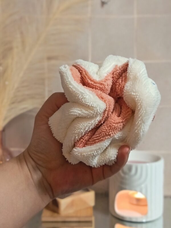 Gros plan d'une fleur de douche bicolore pêche et crème tenue dans une main, illustrant sa texture douce en éponge de bambou.