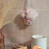 Fleur de bain éco-responsable coloris rose poudré, suspendue par sa cordelette blanche dans un décor de bien-être.