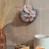 Fleur de douche en tissu rose tendre et filet gris anthracite, mise en scène avec des éléments de décoration bohème chic.