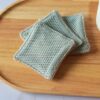 Duo de textures pour ces lingettes lavables : un filet exfoliant vert d'eau monté sur une base en tissu éponge coloris taupe.