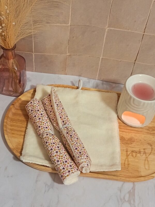 Duo de petites serviettes visage multi-usages en bambou, enroulées pour montrer un délicat motif de petites fleurs champêtres ocre et mauves sur fond blanc.