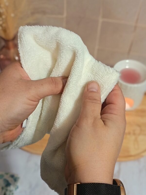 Gros plan de mains manipulant la serviette en bambou de couleur crème pour illustrer la texture moelleuse, douce et absorbante du tissu éponge.