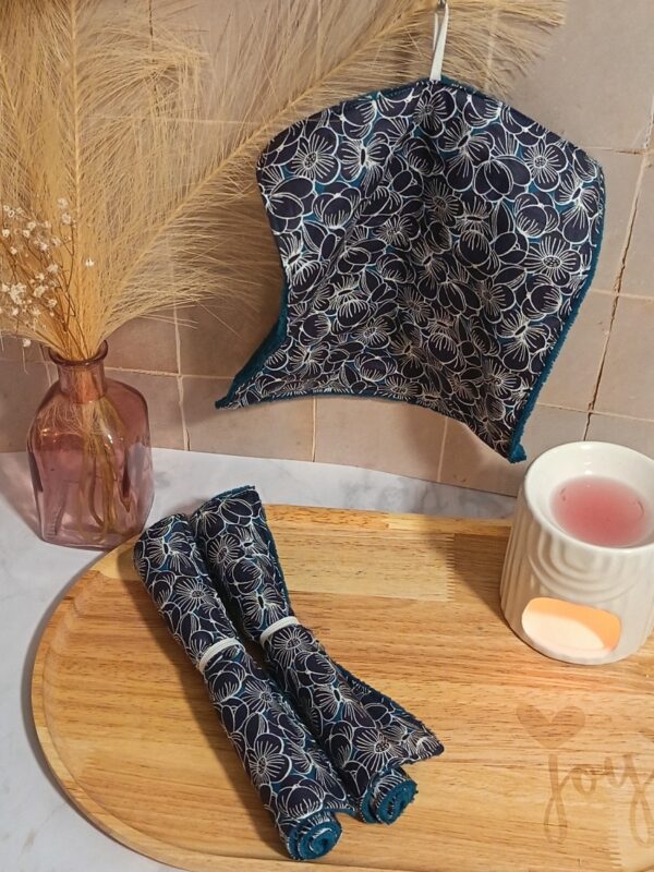 Serviette visage écologique suspendue, montrant un élégant tissu bleu marine aux motifs de fleurs blanches. Le revers en éponge de bambou bleu canard est visible sur les bords.