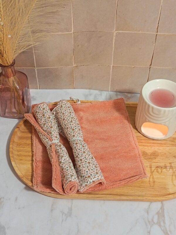Serviettes de soin visage enroulées aux motifs de petites fleurs, présentées sur une éponge en bambou moelleuse coloris pêche.