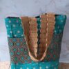 Sac cabas artisanal éco-responsable au style rétro. Le corps du sac mélange un tissu chenille bleu canard à pois beiges et un tissu jacquard à motifs géométriques hexagonaux marron et turquoise. Grandes anses tressées en paille naturelle.