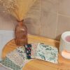 Éventail de lingettes démaquillantes lavables avec différents motifs fleuris et géométriques, disposé sur un plateau en bois dans une ambiance cocooning avec un vase de fleurs séchées.