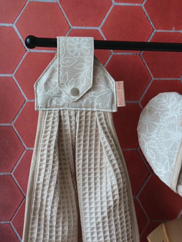 Zoom sur la texture absorbante du nid d'abeille lin et l'imprimé fleuri de l'essuie-main suspendu.