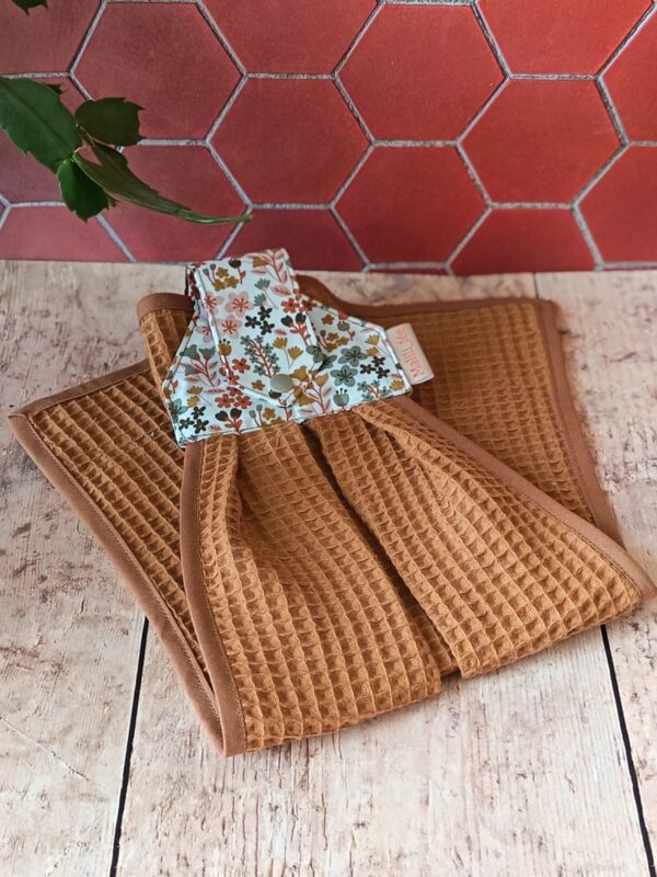 Essuie-main suspendu présenté plié, mettant en avant l'harmonie entre le tissu caramel et l'imprimé floral rose thé.