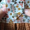 Gros plan sur la patte d'attache en coton fleuri Milly d'un essuie-main suspendu artisanal, vue sur le bouton pression fermé.