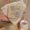 Vue détaillée du filet à savon écologique tenu dans la paume d'une main. On aperçoit le cordon de serrage en coton qui permet de fermer hermétiquement le sachet pour protéger le savon.