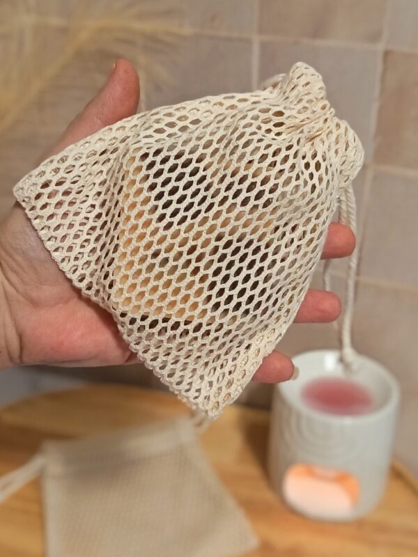 Vue détaillée du filet à savon écologique tenu dans la paume d'une main. On aperçoit le cordon de serrage en coton qui permet de fermer hermétiquement le sachet pour protéger le savon.