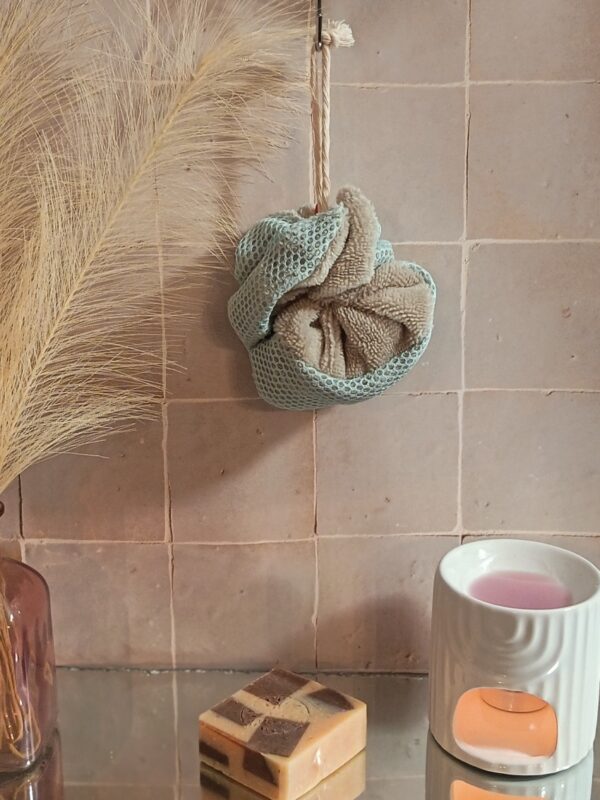 Fleur de douche lavable combinant un tissu éponge taupe et un filet de maintien vert d'eau, ambiance spa.