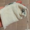 Gros plan sur la texture douce d'un gant sauve-savon en éponge de bambou de couleur crème, tenu à la main pour montrer la souplesse du tissu et son cordon de serrage.