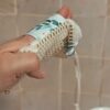 Zoom sur un gant sauve-savon porté à la main, montrant la texture alvéolée du filet en coton bio et une bande de tissu aux motifs de feuilles d'eucalyptus.