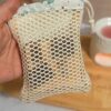 Gant sauve-savon tenu à la main contenant un reste de savon solide visible à travers le filet de coton, idéal pour utiliser ses savons jusqu'au bout sans gaspillage.