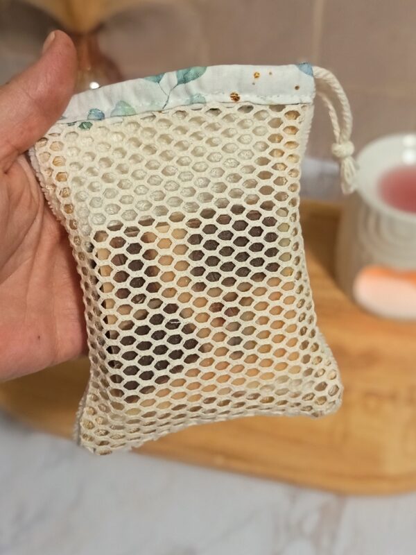 Gant sauve-savon tenu à la main contenant un reste de savon solide visible à travers le filet de coton, idéal pour utiliser ses savons jusqu'au bout sans gaspillage.