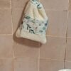 Gant sauve-savon suspendu par son cordon contre un mur en carrelage beige, démontrant une solution de séchage rapide et hygiénique pour la salle de bain.