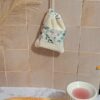 Gant sauve-savon suspendu par son cordon contre un mur en carrelage beige, démontrant une solution de séchage rapide et hygiénique pour la salle de bain.
