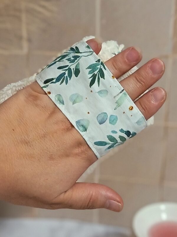 Vue détaillée de la lanière de maintien d'un gant sauve-savon passée sur le dos de la main, assurant une prise en main stable et confortable pendant la douche.