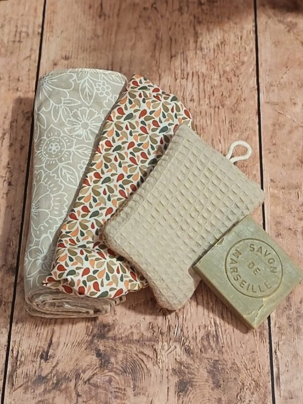 Kit cuisine zéro déchet comprenant un rouleau d'essuie-tout lavable fleuri, un couvre-plat en tissu assorti, une éponge réutilisable beige et un cube de savon de Marseille.