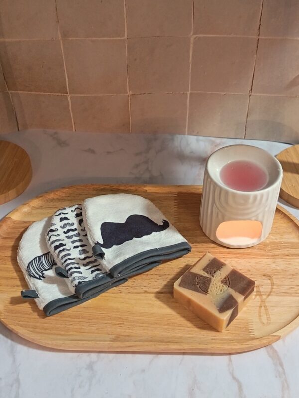 Lingettes lavables en forme de gants avec imprimé "Moustache" et une grande moustache noire centrale, présentées avec un savon bicolore et un diffuseur d'ambiance.