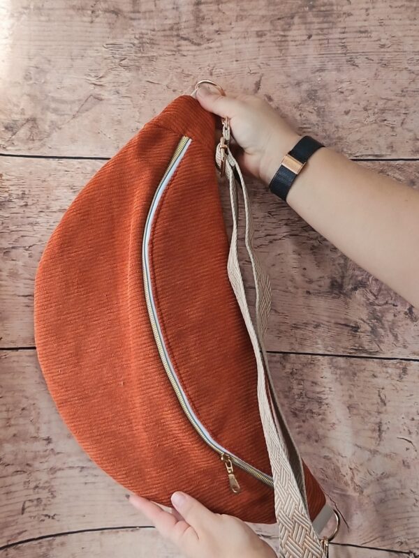 Gros plan sur les mains tenant le sac banane terracotta pour montrer sa grande taille et la souplesse du velours côtelé.