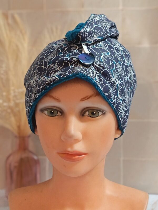 Serviette à cheveux turban avec doublure en éponge de bambou bleu pétrole et tissu extérieur à motifs de fleurs blanches sur fond bleu foncé.