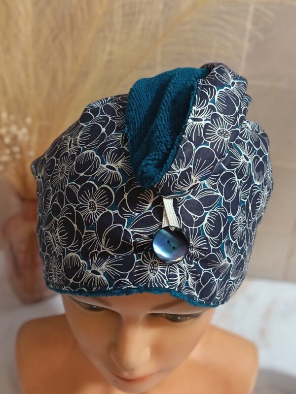 Détail de la serviette à cheveux bleu pétrole montrant le bouton nacré foncé et la texture moelleuse de l'éponge de bambou colorée.