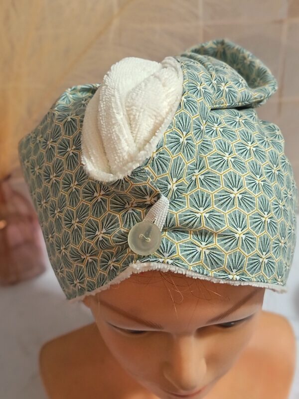 Turban serviette à cheveux en éponge de bambou blanche et tissu à motifs géométriques d'éventails verts et dorés avec bouton transparent.