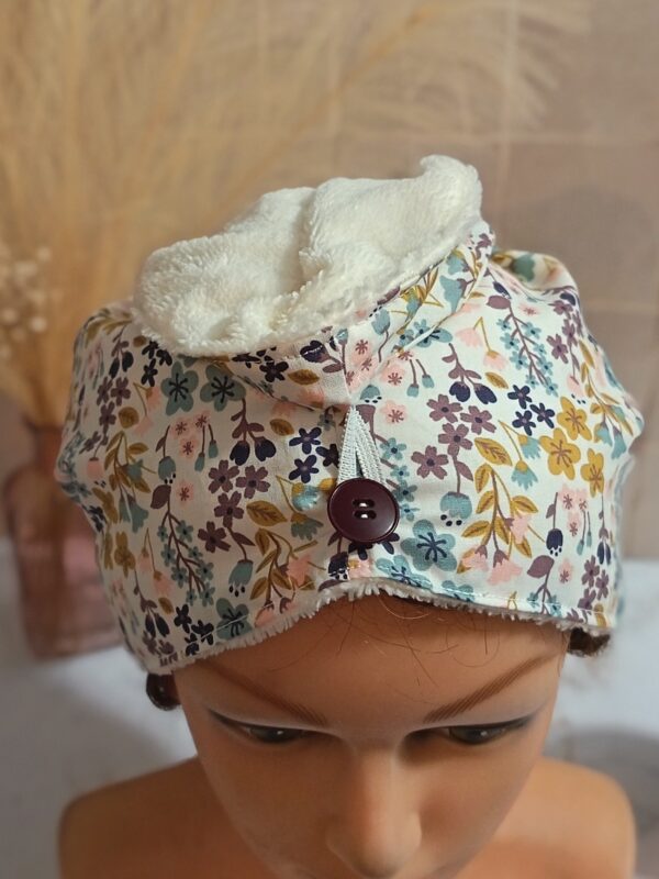 Détail de l'attache élastique sur bouton violet d'une serviette à cheveux artisanale, montrant le tissu fleuri et la doublure en éponge blanche.