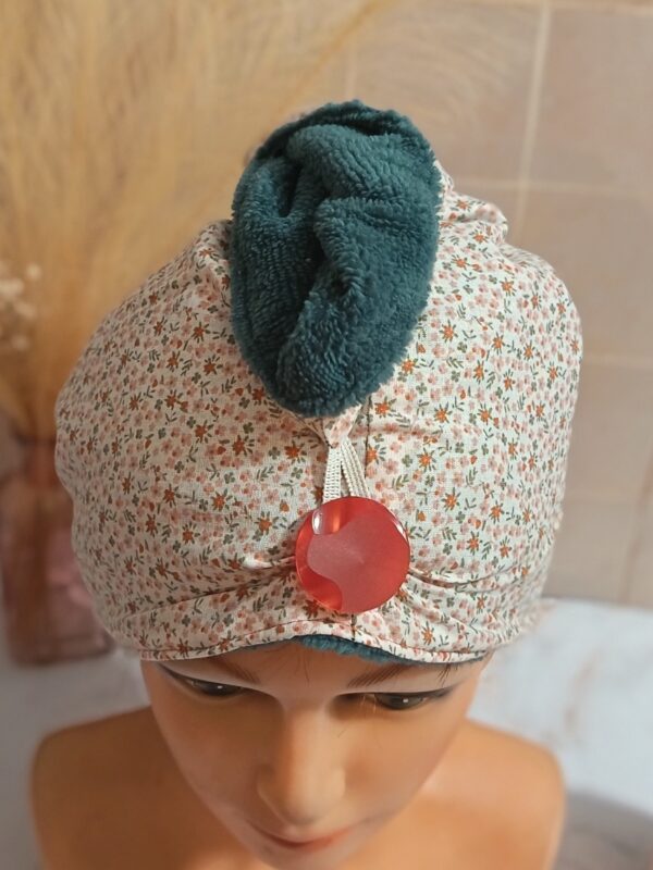 "Gros plan sur une serviette à cheveux montrant le contraste entre le tissu floral délicat, l'éponge de bambou vert foncé et un gros bouton rouge brillant.