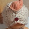 Zoom sur la texture d'une serviette à cheveux : éponge de bambou rose pêche ultra-douce et attache élastique sur bouton rond bordeaux.