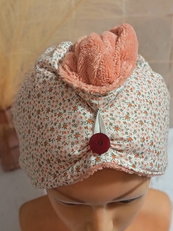 Zoom sur la texture d'une serviette à cheveux : éponge de bambou rose pêche ultra-douce et attache élastique sur bouton rond bordeaux.