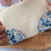Main tenant une pochette artisanale en tissu écru, illustrant sa taille idéale pour un usage nomade.