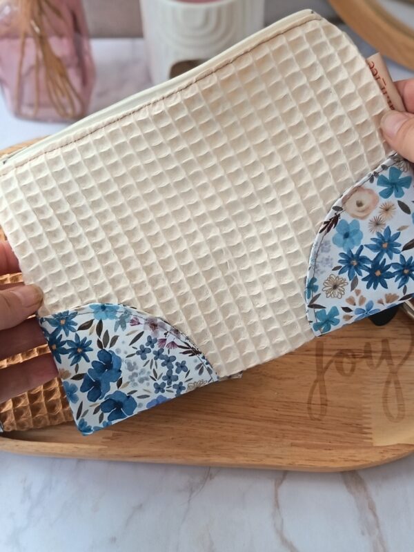 Main tenant une pochette artisanale en tissu écru, illustrant sa taille idéale pour un usage nomade.