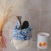 Panier de rangement en tissu crème utilisé comme organiseur de salle de bain avec brosses à cheveux et lingettes démaquillantes.