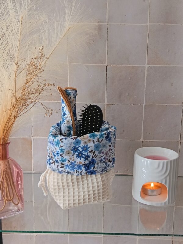 Panier de rangement en tissu crème utilisé comme organiseur de salle de bain avec brosses à cheveux et lingettes démaquillantes.