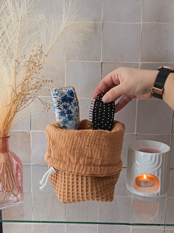 Organiseur en tissu ocre et gaze de coton dorée, replié pour laisser apparaître le contenu (brosse et accessoires de beauté).