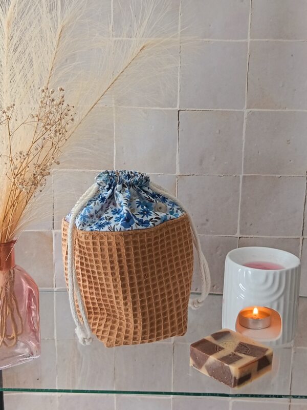 Petit pochon de rangement en coton nid d'abeille coloris ocre, doublure fleurie bleue et cordon de serrage blanc.