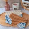 Deux pochettes de rangement artisanales en tissu nid d'abeille ocre et écru avec coins fleuris, posées sur un plateau en bois.