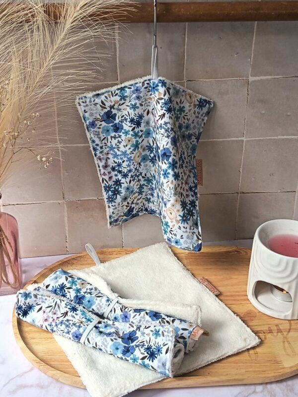 Serviettes visage réutilisables avec une face en coton fleuri bleu et une face en éponge blanche ultra-douce. Une serviette est suspendue par son attache pour séchage.