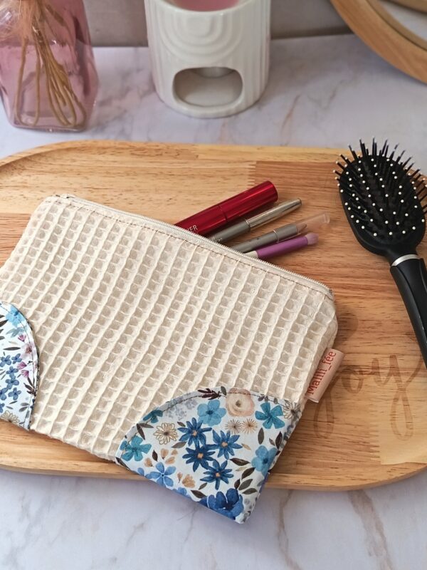 Pochette en nid d'abeille écru utilisée comme trousse à maquillage avec mascara et pinceaux sur un plateau.