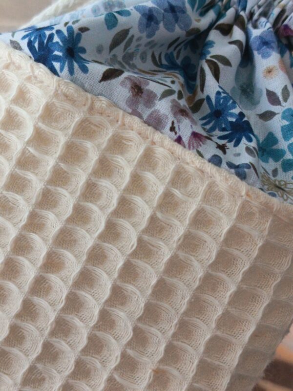 Gros plan sur les textures : tissu nid d'abeille écru et coton imprimé floral bleu de la collection Douceur Ocre Bleutée.