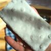 Gros plan montrant la texture douce et texturée de la face en tissu minky blanc d'un essuie-lunettes artisanal, tenu entre les doigts.