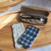 Gros plan sur un essuie-lunettes tissu double gaze vichy bleu et blanc, posé à côté de sa face minky blanche sur un plateau en bois.